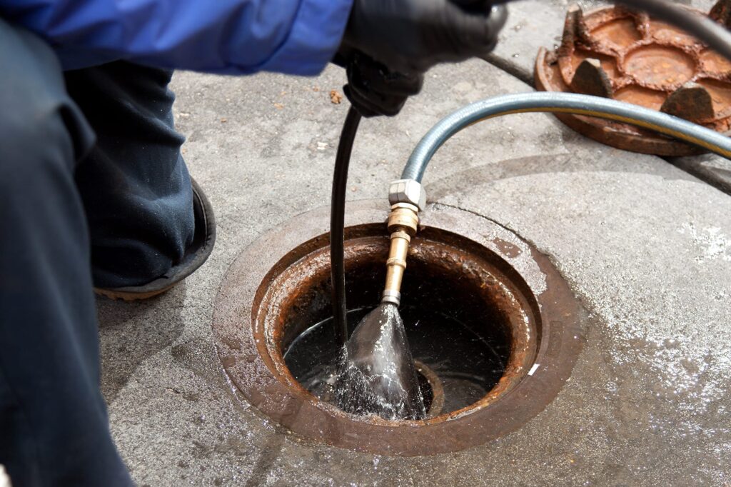 Plumber hydro jetting a sewer line through a manhole in Roswell