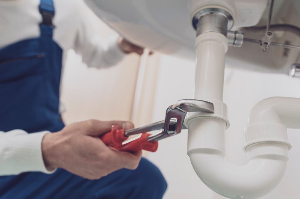 Plumber repairing a white drain pipe beneath a sink in Roswell
