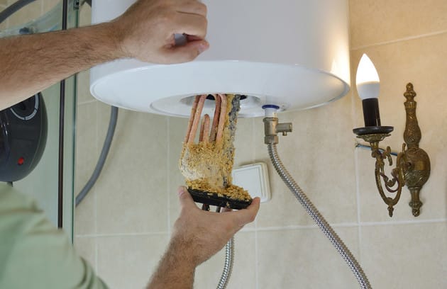 Technician removing mineral buildup from a water heater in Roswell